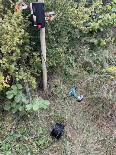 Elstängsel aggregat i olika styrka En elektrisk apparat står vid en stolpe, med en borrmaskin och en kabel på marken.