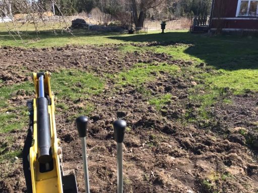 reparation av bökskador på gräsmatta Gräsmatta med nyligen bearbetad jord och en grävmaskin i förgrunden.