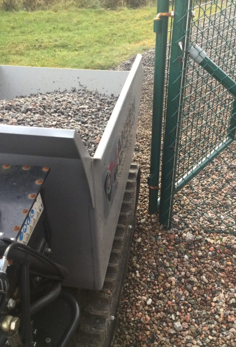 utkörning och inkörning av olika material minidumper med grus står bredvid en öppen grind på grusad gång.